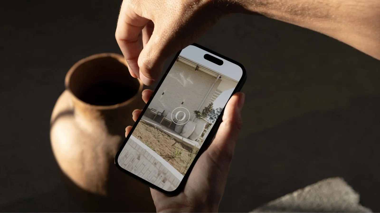 Hand holding a phone showing The Orchard website, with the venue's courtyard behind the O logo