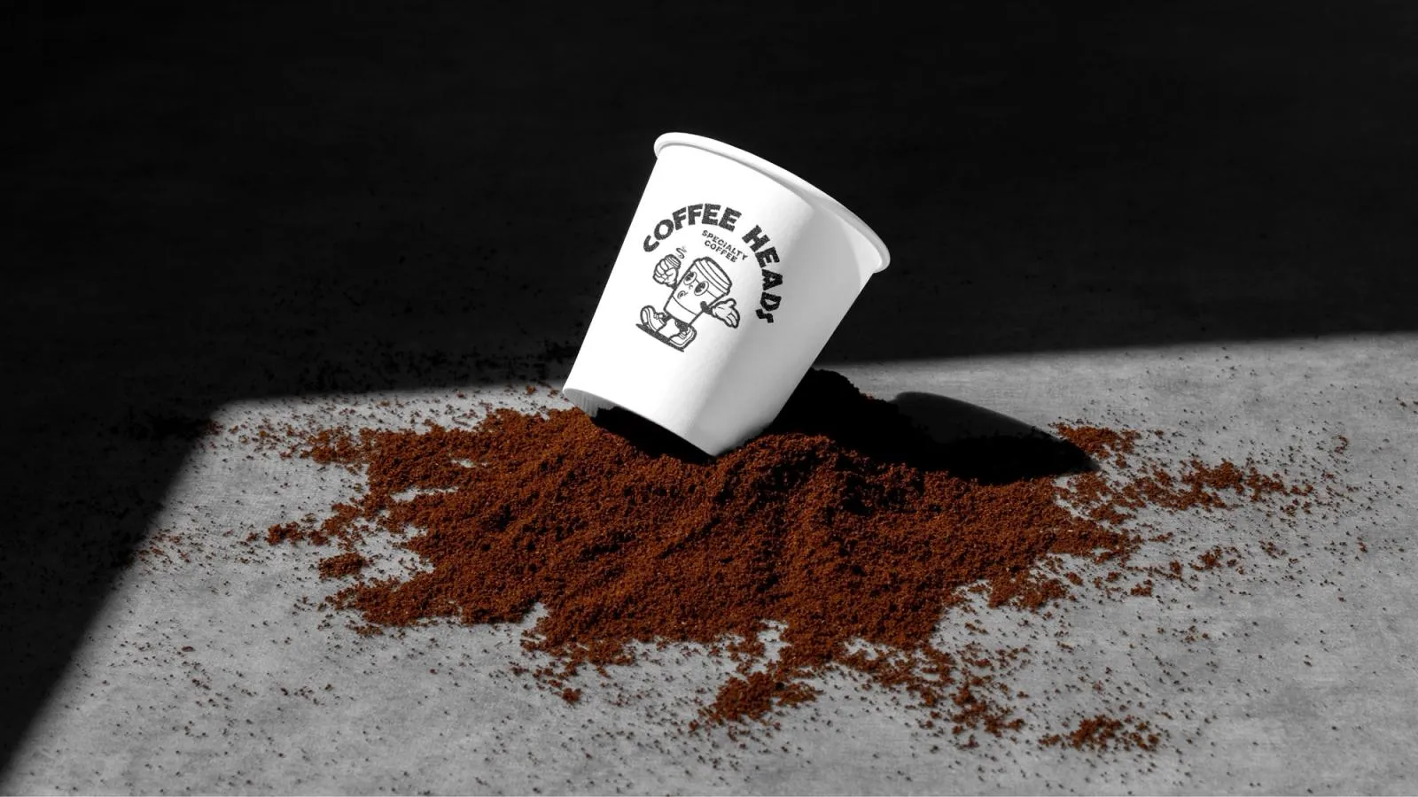 Coffee Heads branded takeaway cup tipped over in a spill of ground coffee