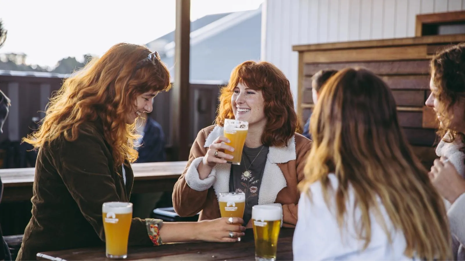 Friends laughing over pints of hazy pale ale at the bar of a Mountain Culture brewery venue