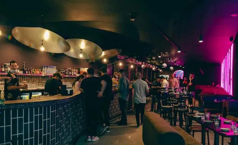 Crowd at the bar of Duck Duck Goose in Penrith, lit by pink neon and gold pendant lights