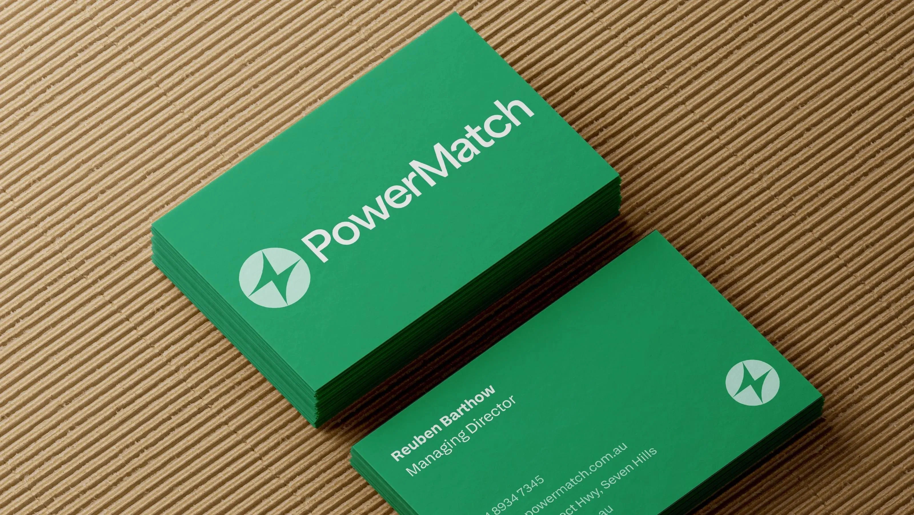 Stacked green PowerMatch business cards with the lightning bolt logo, on corrugated card