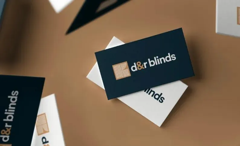 Navy and white D&R Blinds business cards with the copper square logo, scattered across a desk