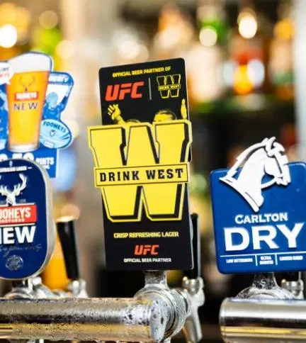 Drink West UFC tap badge on a pub bar, pouring alongside Tooheys New and Carlton Dry