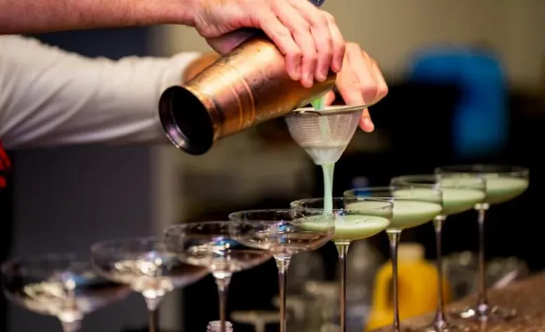 Bartender straining a pale green cocktail into a row of coupe glasses at The Flower Shop Penrith