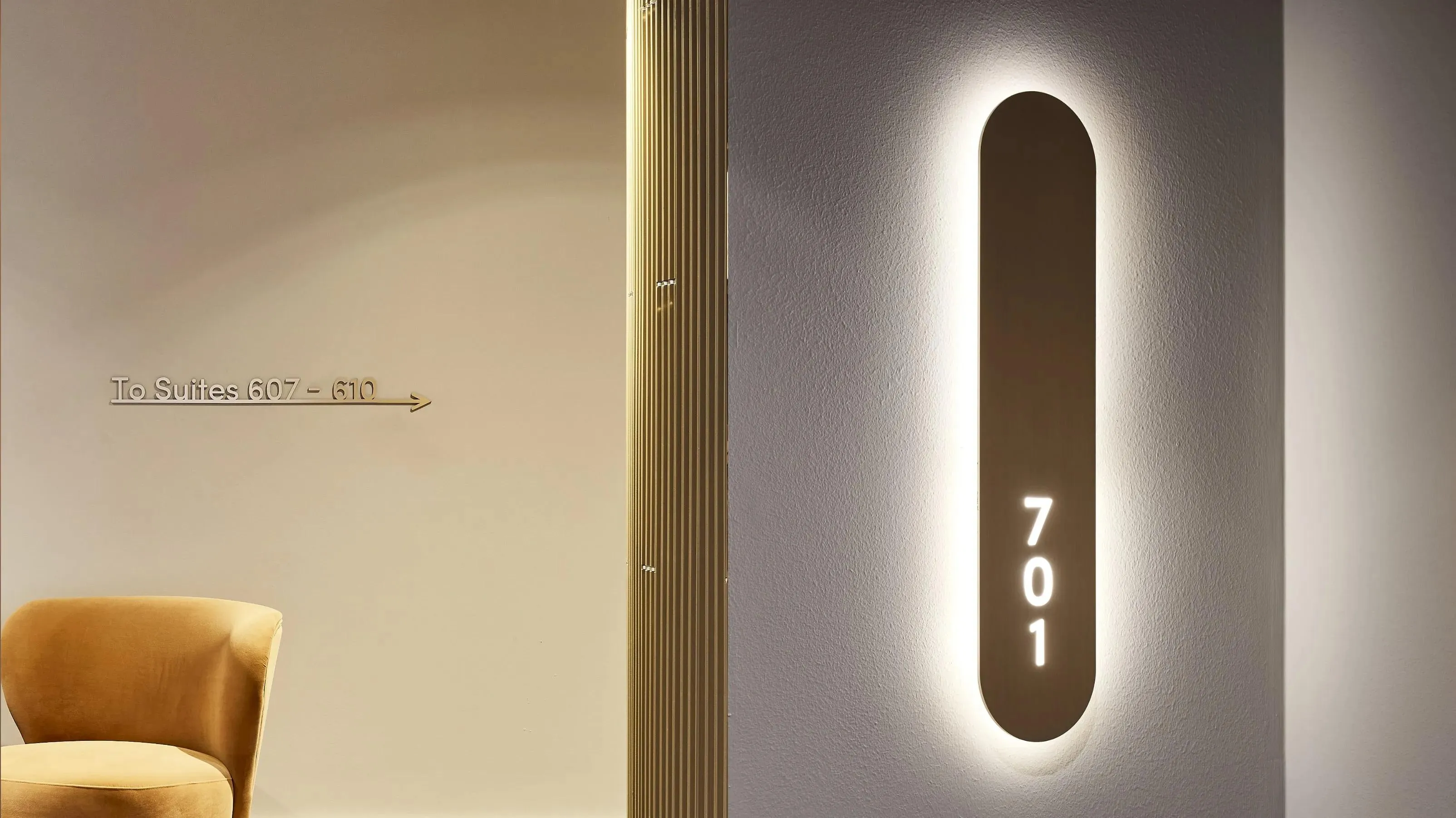 Astina Suites corridor wayfinding: brass suite directions and a backlit room number sign