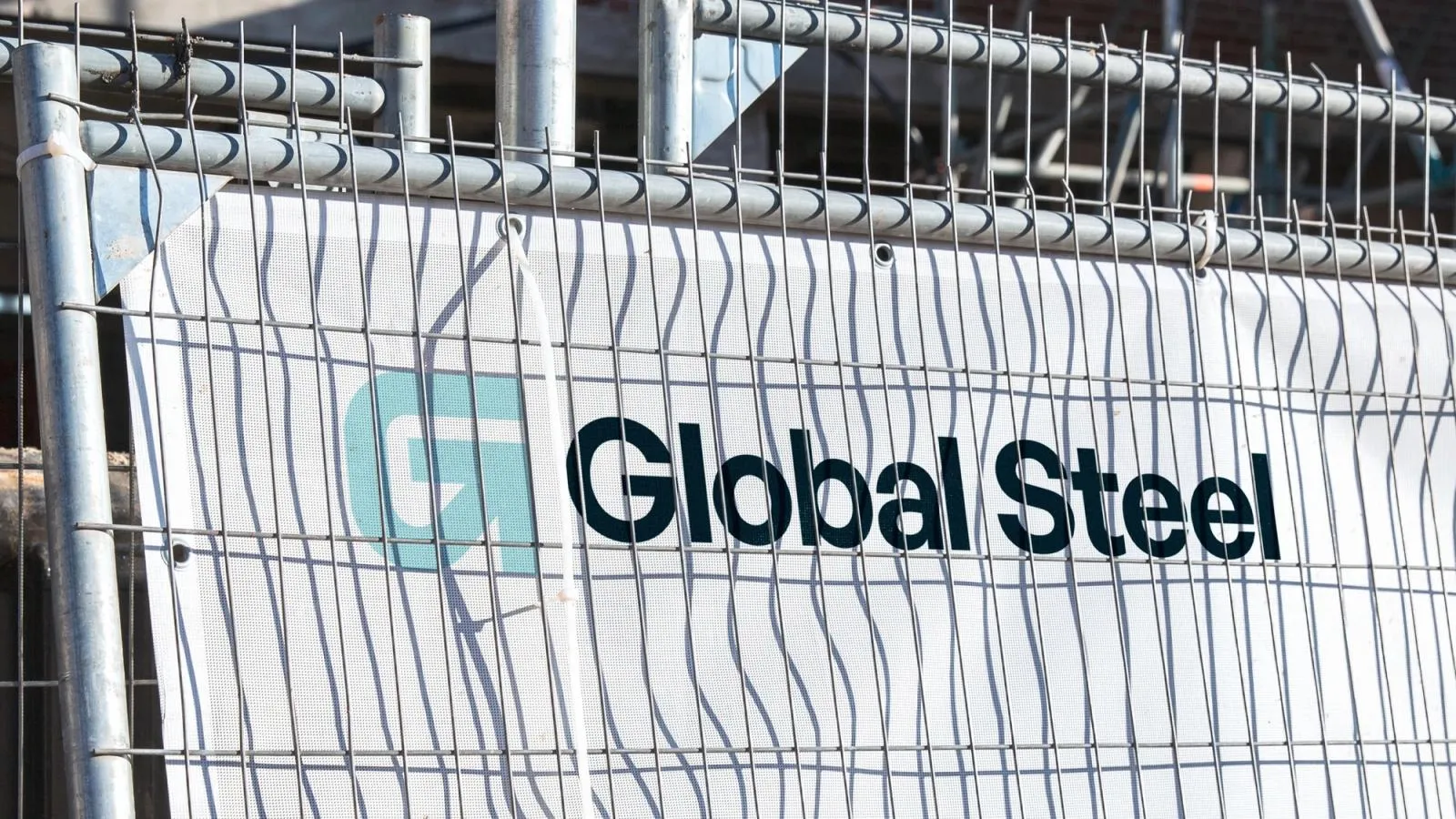 Global Steel banner with the G arrow logo, zip-tied to temporary construction site fencing