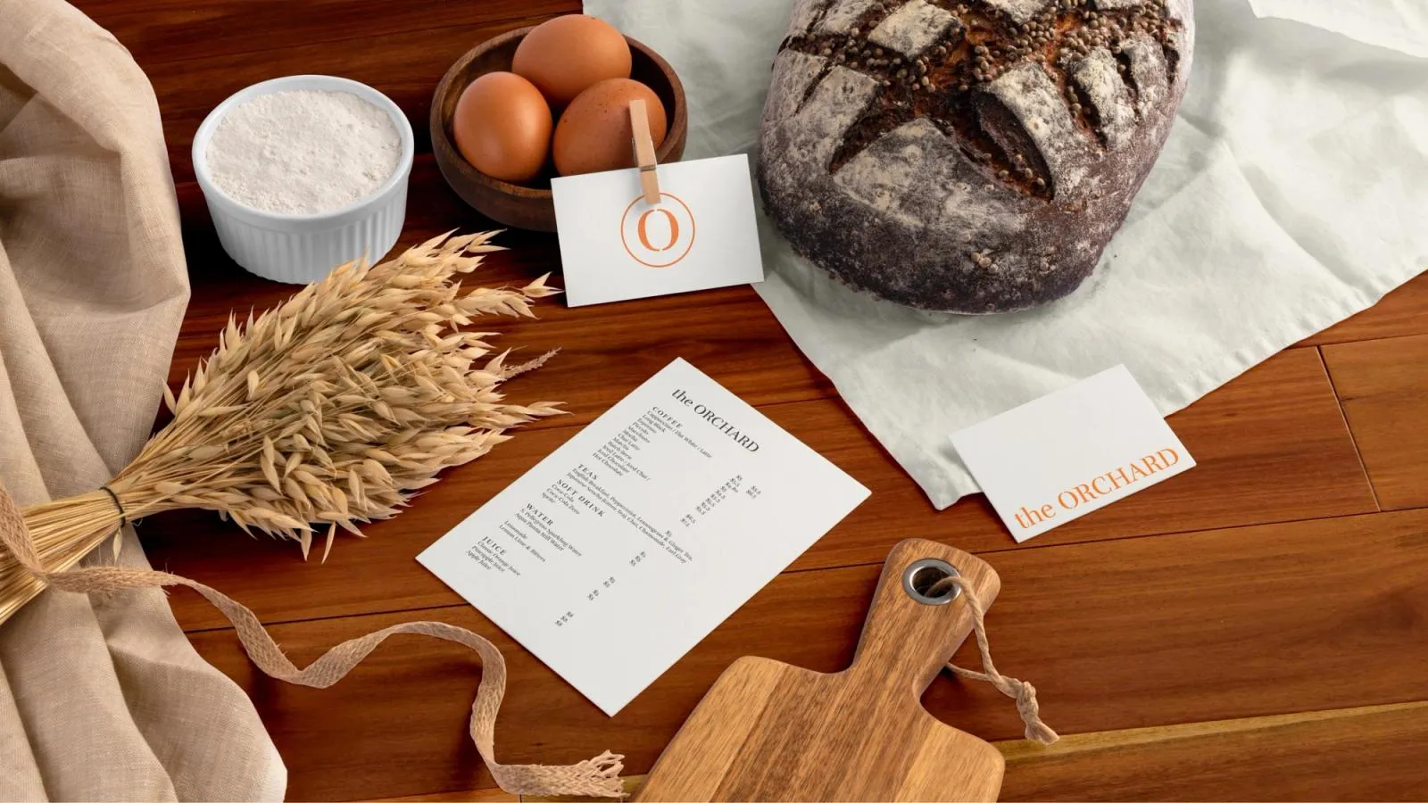 The Orchard menu and cards styled on a table with sourdough, eggs, flour and wheat