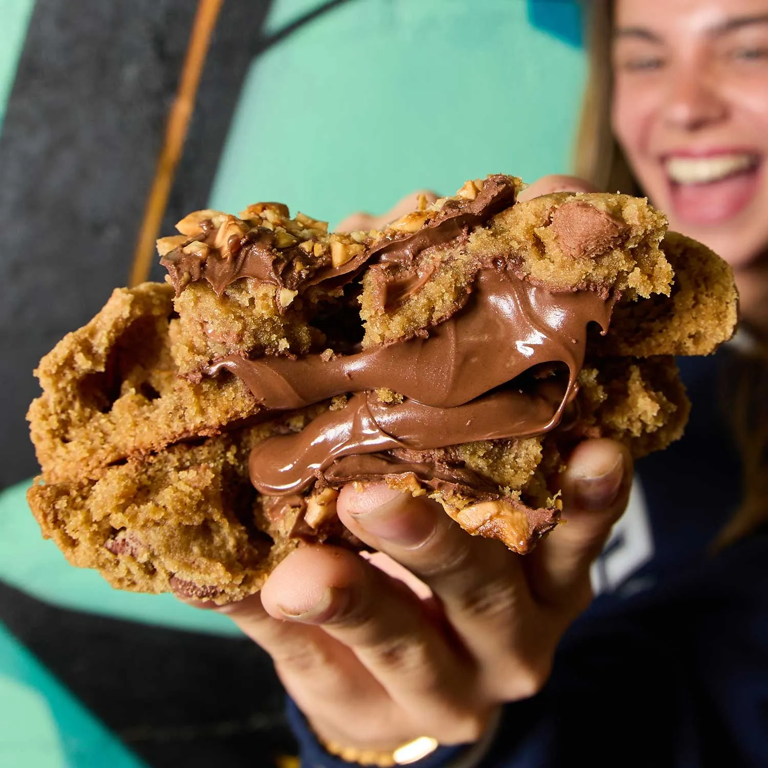 Hand holding a Cookieman cookie split open with melted chocolate filling, laughing woman behind