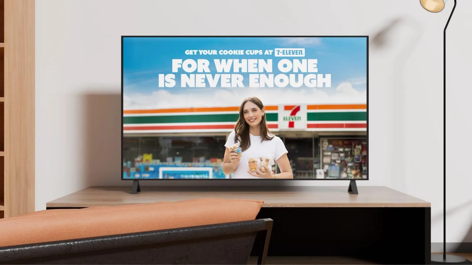 Cookieman TV spot on a living room screen: "For when one is never enough", cookie cups at 7-Eleven