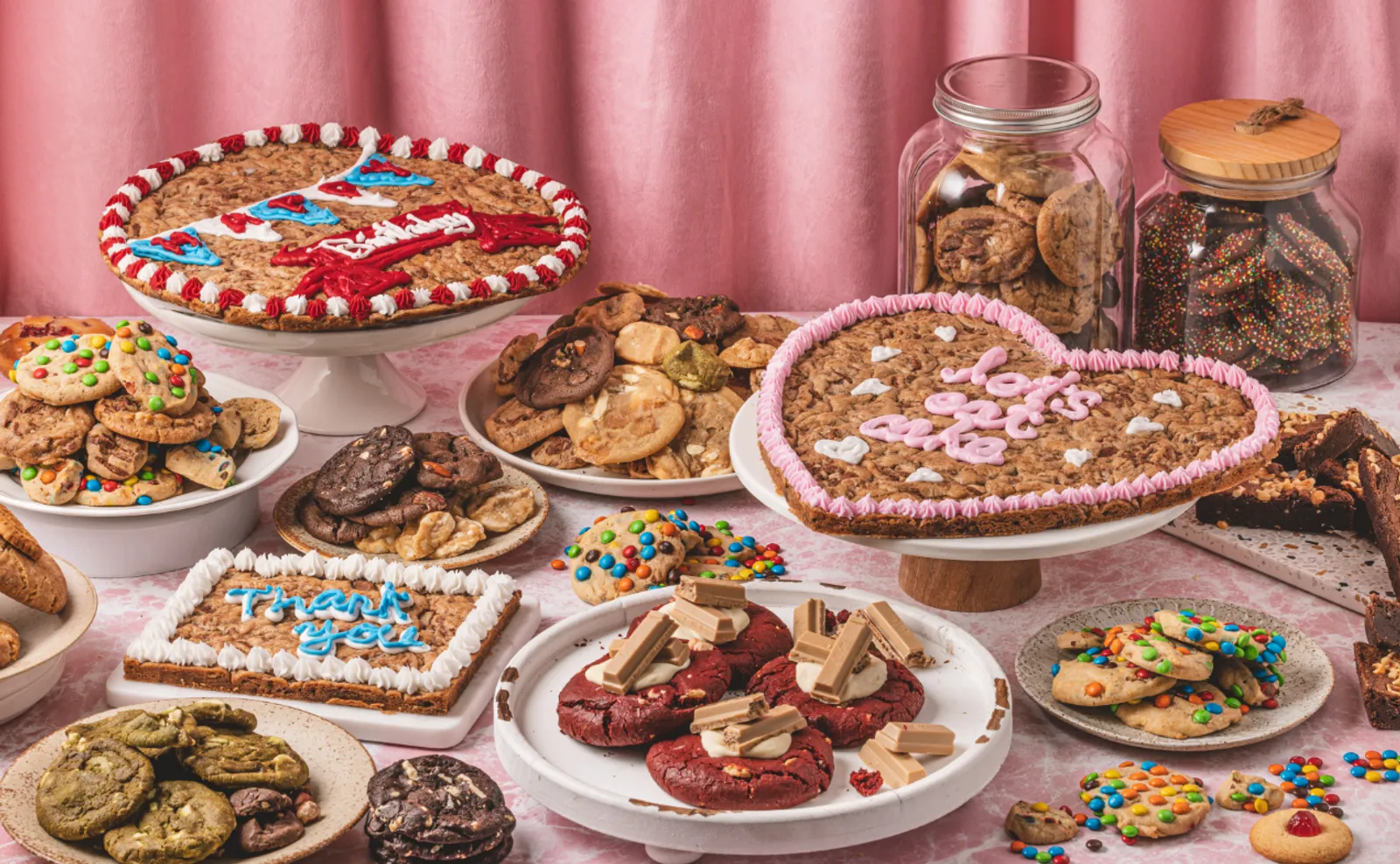 Iced cookie cakes for birthdays and thank-yous spread across a table of Mrs Fields cookies and treats