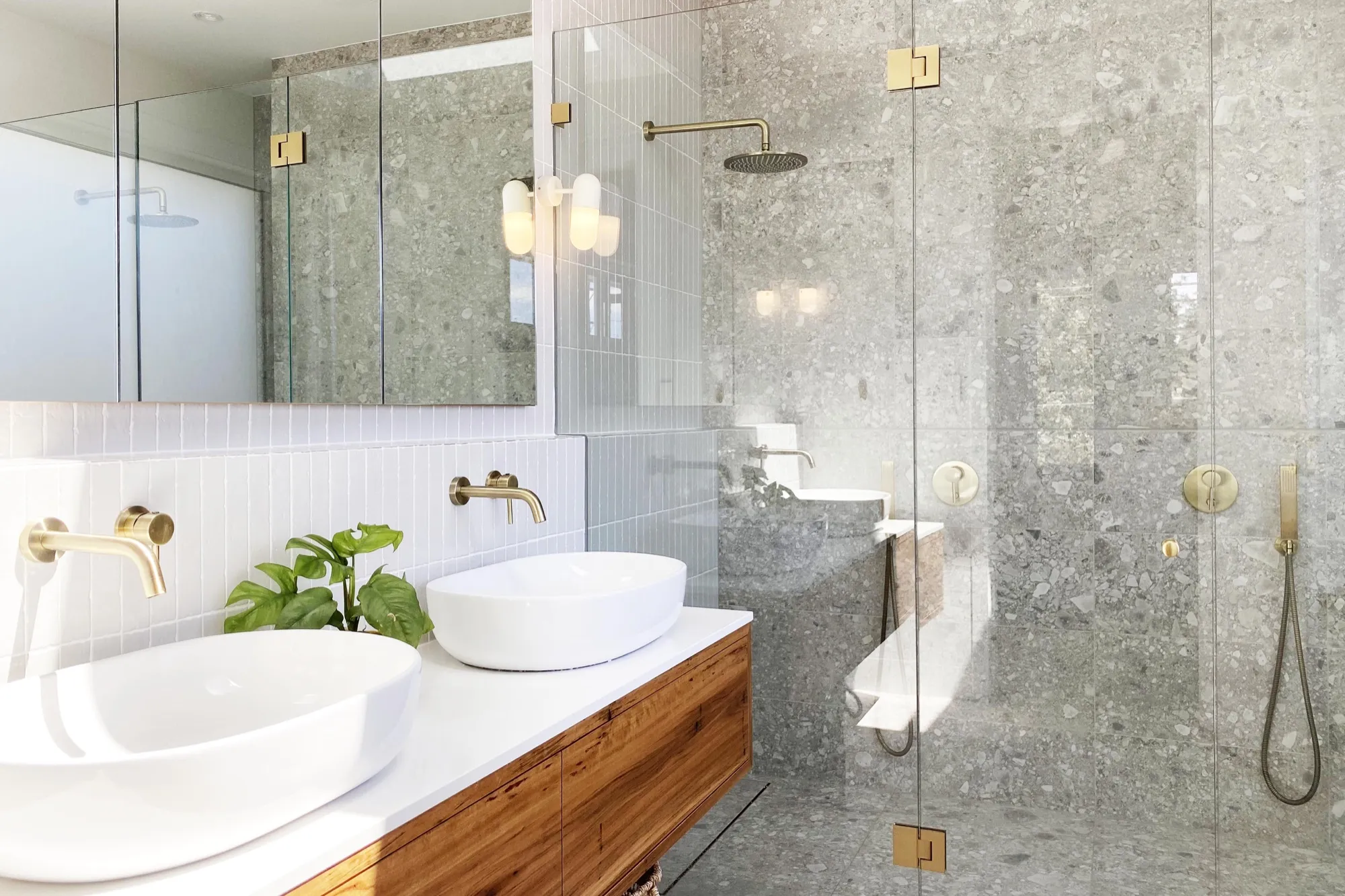Bathroom with grey terrazzo-look tiles, double vanity on timber and brushed brass tapware